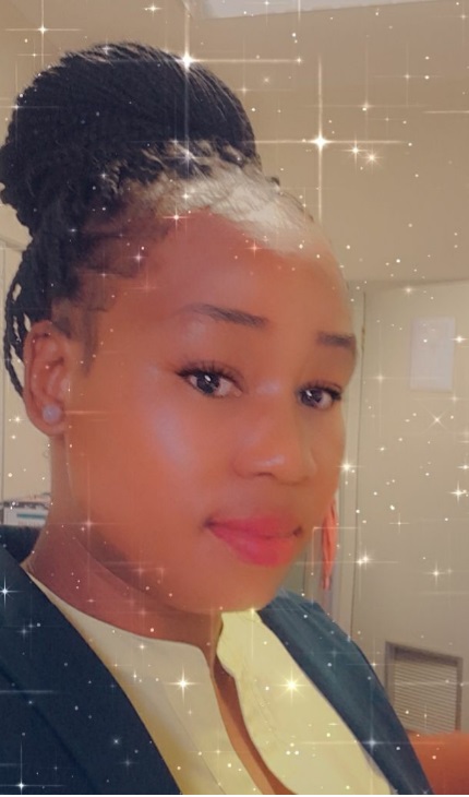 Head shot of a dark skinned lady whose braided black hair is tied up in a bun on top of her head. She is wearing a stud earing, a Chinese neck cream shirt and a navy blue jacket